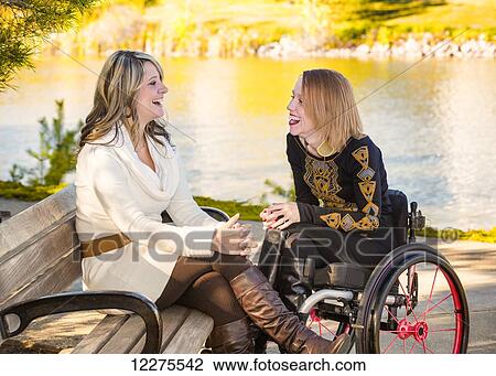 Stock Image - Young paraplegic woman and her friend spending quality time together in a city park in autumn; Edmonton, Alberta, Canada. Fotosearch