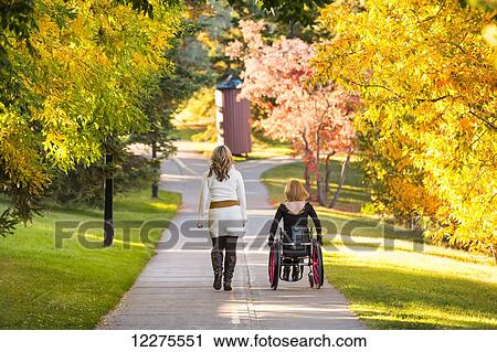Stock Image - Young paraplegic woman and her friend spending quality time together in a city park in autumn; Edmonton, Alberta, Canada. Fotosearch