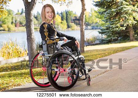 Stock Image - Young paraplegic woman in her wheelchair on a path in a city park in autumn; Edmonton, Alberta, Canada. Fotosearch