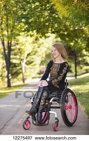 Stock Photo - Young paraplegic woman in her wheelchair on a path in a city park in autumn; Edmonton, Alberta, Canada. Fotosearch
