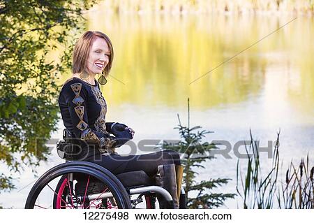 Stock Photo - Young paraplegic woman in her wheelchair by water in a city park in autumn; Edmonton, Alberta, Canada. Fotosearch