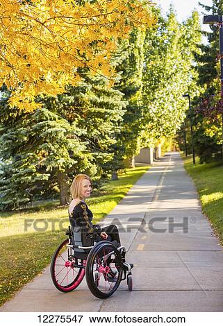 Stock Photo - Young paraplegic woman in her wheelchair on a path in a city park in autumn; Edmonton, Alberta, Canada. Fotosearch