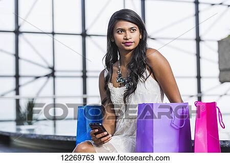 Stock Image - Young professional businesswoman in downtown building with shopping bags; Edmonton, Alberta, Canada. Fotosearch