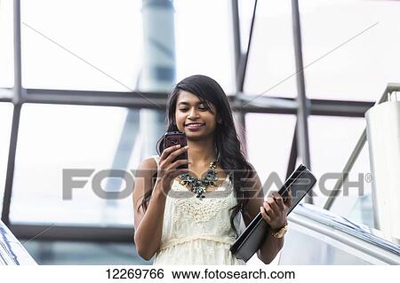 Young professional businesswoman texting on her smart phone on escalator; Edmonton, Alberta, Canada View Large Photo Image Stock Photograph - Young professional businesswoman texting on her smart phone on escalator; Edmonton, Alberta, Canada. Fotosearch