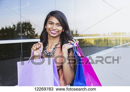 Stock Image - Young professional businesswoman with shopping bags in downtown setting; Edmonton, Alberta, Canada. Fotosearch