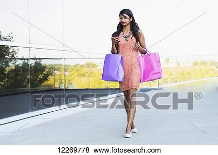 Young professional businesswoman with shopping bags and checking her smart phone in downtown urban setting; Edmonton, Alberta, Canada View Large Photo Image Stock Photo - Young professional businesswoman with shopping bags and checking her smart phone in downtown urban setting; Edmonton, Alberta, Canada. Fotosearch