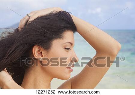 Stock Image - Young woman in white dress on the beach at the water's edge; Kailua, Island of Hawaii, Hawaii, United States of America. Fotosearch