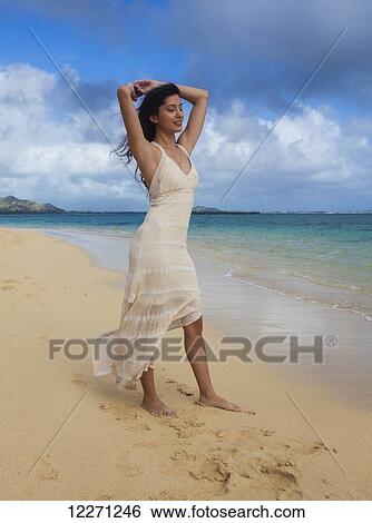 Stock Photograph - Young woman in white dress on the beach at the water's edge; Kailua, Island of Hawaii, Hawaii, United States of America. Fotosearch