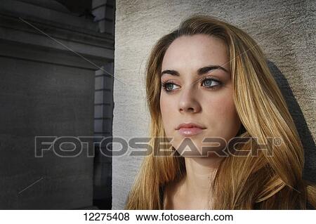 Stock Photo - Young woman leaning against a stone pillar, eyes diverted from the camera with no smile on her face; United States of America. Fotosearch
