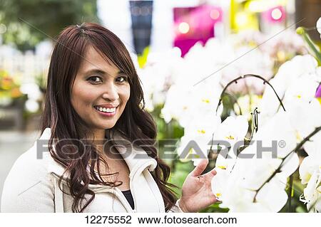 Young woman looking at flowers in a greenhouse; St. Albert, Alberta, Canada View Large Photo Image Stock Image - Young woman looking at flowers in a greenhouse; St. Albert, Alberta, Canada. Fotosearch