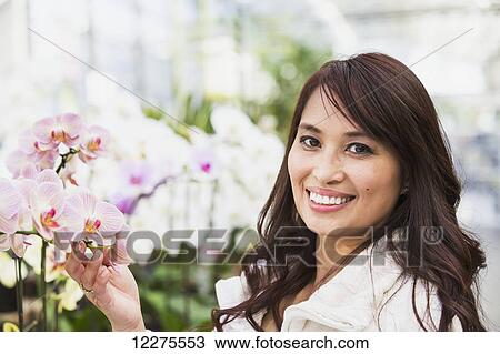 Stock Image - Young woman looking at flowers in a greenhouse; St. Albert, Alberta, Canada. Fotosearch