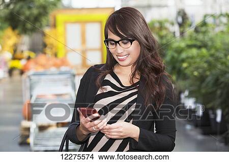 Picture - Young woman shopping at a mall and checking her cell phone for messages; St. Albert, Alberta, Canada. Fotosearch