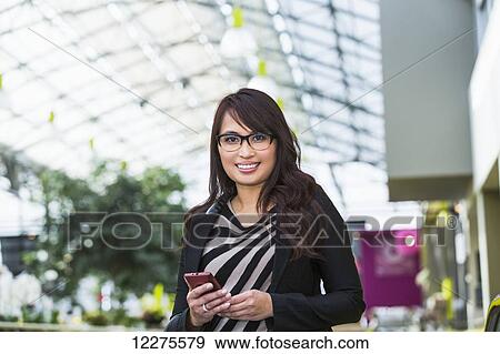 Stock Photo - Young woman shopping at a mall and checking her cell phone for messages; St. Albert, Alberta, Canada. Fotosearch
