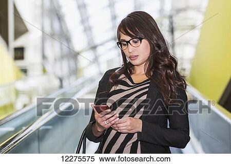 Stock Photography - Young woman shopping at a mall and checking her cell phone for messages; St. Albert, Alberta, Canada. Fotosearch