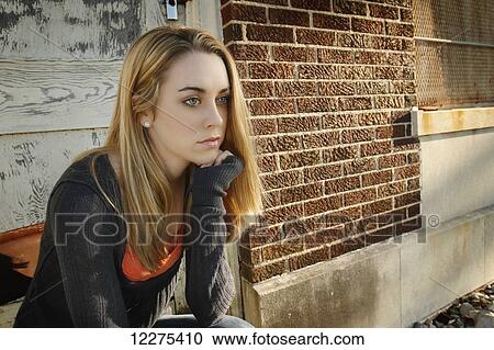 Stock Image - Young woman sitting in a chair outside of a building, looking unhappy; United States of America. Fotosearch