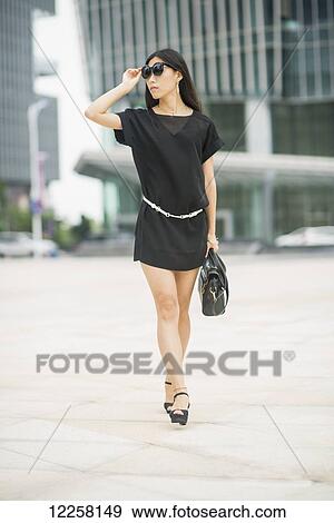 Stock Photo - Young woman walking in business district; Xiamen, China. Fotosearch