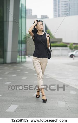 Stock Photo - Young woman walking in business district; Xiamen, China. Fotosearch