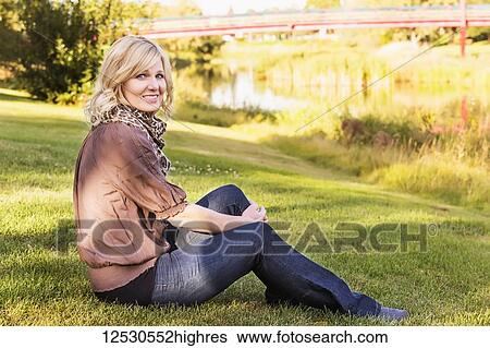 A beautiful blonde middle-aged woman poses for the camera while relaxing beside a river in a park on a warm fall evening; St. Alberta, Alberta, Canada View Large Photo Image Stock Photograph - A beautiful blonde middle-aged woman poses for the camera while relaxing beside a river in a park on a warm fall evening; St. Alberta, Alberta, Canada. Fotosearch