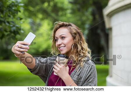 Stock Photograph - A beautiful female university student taking a self-portrait with her smart phone on the campus; Edmonton, Alberta, Canada. Fotosearch