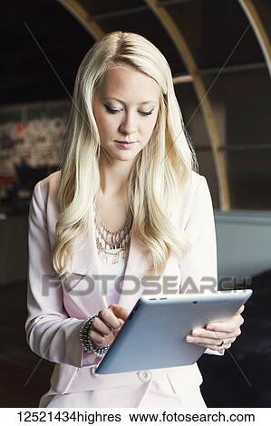 Stock Photograph - A beautiful young millennial business woman with long blond hair in the workplace using technology; Sherwood Park, Alberta, Canada. Fotosearch