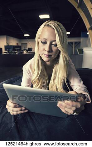Stock Photograph - A beautiful young millennial business woman with long blond hair in the workplace using technology; Sherwood Park, Alberta, Canada. Fotosearch