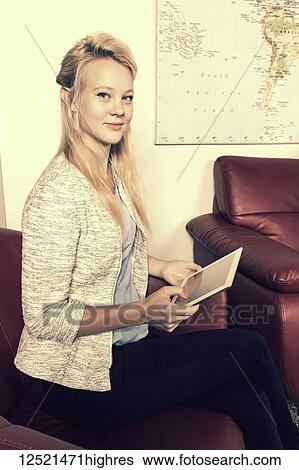Stock Photograph - A beautiful young millennial business woman with long blond hair using her tablet in the lobby of a workplace while waiting for a job interview; Sherwood Park, Alberta, Canada. Fotosearch