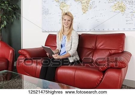 Stock Photograph - A beautiful young millennial business woman with long blond hair using her tablet in the lobby of a workplace while waiting for a job interview and posing for the camera; Sherwood Park, Alberta, Canada. Fotosearch
