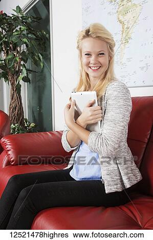 Stock Photograph - A beautiful young millennial business woman with long blond hair using her tablet in the lobby of a workplace while waiting for a job interview and posing for the camera; Sherwood Park, Alberta, Canada. Fotosearch