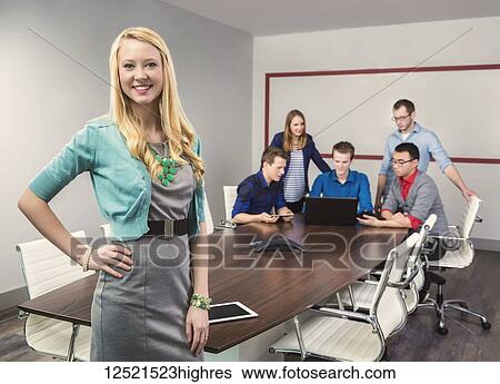 Stock Photograph - A beautiful young millennial business woman working on her tablet in a conference room with her co-workers; Sherwood Park, Alberta, Canada. Fotosearch