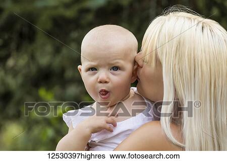 A beautiful young mom cuddling her baby daughter who is making a funny face while enjoying quality time together outdoors in a park on a warm summer day; Edmonton, Alberta, Canada View Large Photo Image Stock Photograph - A beautiful young mom cuddling her baby daughter who is making a funny face while enjoying quality time together outdoors in a park on a warm summer day; Edmonton, Alberta, Canada. Fotosearch