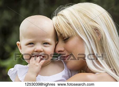 A beautiful young mom cuddling her baby daughter while enjoying quality time together outdoors in a park on a warm summer day; Edmonton, Alberta, Canada View Large Photo Image Stock Photograph - A beautiful young mom cuddling her baby daughter while enjoying quality time together outdoors in a park on a warm summer day; Edmonton, Alberta, Canada. Fotosearch