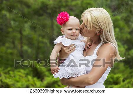 A beautiful young mom cuddling her baby daughter while enjoying quality time together outdoors in a park on a warm summer day; Edmonton, Alberta, Canada View Large Photo Image Stock Photograph - A beautiful young mom cuddling her baby daughter while enjoying quality time together outdoors in a park on a warm summer day; Edmonton, Alberta, Canada. Fotosearch