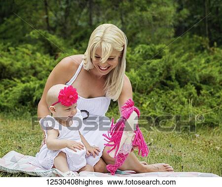 A beautiful young mother enjoying quality time with her cute baby daughter sitting on a blanket and playing with a doll in a city park on a summer day; Edmonton, Alberta, Canada. View Large Photo Image Stock Photograph - A beautiful young mother enjoying quality time with her cute baby daughter sitting on a blanket and playing with a doll in a city park on a summer day; Edmonton, Alberta, Canada.. Fotosearch