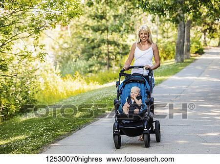 A beautiful young mother taking her baby daughter out for a walk using a stroller in a park with a lake on a warm sunny day; Edmonton, Alberta, Canada View Large Photo Image Stock Photograph - A beautiful young mother taking her baby daughter out for a walk using a stroller in a park with a lake on a warm sunny day; Edmonton, Alberta, Canada. Fotosearch