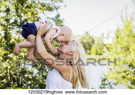 A beautiful young mother with long blonde hair enjoying quality time with her cute baby daughter and tossing her in the air in a city park on a summer day; Edmonton, Alberta, Canada View Large Photo Image Stock Photograph - A beautiful young mother with long blonde hair enjoying quality time with her cute baby daughter and tossing her in the air in a city park on a summer day; Edmonton, Alberta, Canada. Fotosearch