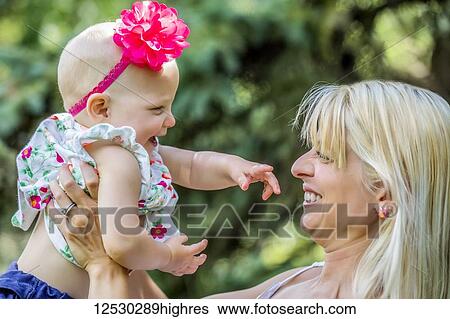 A beautiful young mother with long blonde hair enjoying quality time with her cute baby daughter in a city park on a summer day; Edmonton, Alberta, Canada View Large Photo Image Stock Photograph - A beautiful young mother with long blonde hair enjoying quality time with her cute baby daughter in a city park on a summer day; Edmonton, Alberta, Canada. Fotosearch