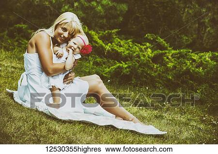 A beautiful young mother with long blonde hair enjoying quality time with her cute baby daughter sitting on a blanket on the grass in a city park on a summer day; Edmonton, Alberta, Canada View Large Photo Image Stock Photograph - A beautiful young mother with long blonde hair enjoying quality time with her cute baby daughter sitting on a blanket on the grass in a city park on a summer day; Edmonton, Alberta, Canada. Fotosearch