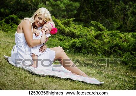 A beautiful young mother with long blonde hair enjoying quality time with her cute baby daughter sitting on a blanket on the grass in a city park on a summer day; Edmonton, Alberta, Canada View Large Photo Image Stock Photograph - A beautiful young mother with long blonde hair enjoying quality time with her cute baby daughter sitting on a blanket on the grass in a city park on a summer day; Edmonton, Alberta, Canada. Fotosearch