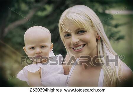 A beautiful young mother with long blonde hair enjoying quality time with her cute baby daughter in a city park on a summer day and posing for the camera; Edmonton, Alberta, Canada View Large Photo Image Stock Photograph - A beautiful young mother with long blonde hair enjoying quality time with her cute baby daughter in a city park on a summer day and posing for the camera; Edmonton, Alberta, Canada. Fotosearch