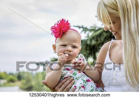 A beautiful young mother with long blonde hair enjoying quality time with her cute baby daughter in a city park on a summer day; Edmonton, Alberta, Canada View Large Photo Image Stock Photograph - A beautiful young mother with long blonde hair enjoying quality time with her cute baby daughter in a city park on a summer day; Edmonton, Alberta, Canada. Fotosearch