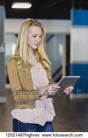 Stock Photograph - A beautiful young professional business woman with long blond hair using technology in the workplace; Sherwood Park, Alberta, Canada. Fotosearch