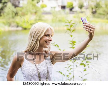 A beautiful young woman taking a self-portrait while enjoying her alone time in a park with a manmade lake; Edmonton, Alberta, Canada View Large Photo Image Stock Photograph - A beautiful young woman taking a self-portrait while enjoying her alone time in a park with a manmade lake; Edmonton, Alberta, Canada. Fotosearch