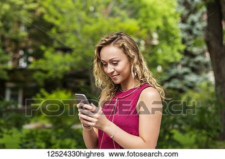 Stock Photograph - A beautiful young woman texting on her smart phone outside on a university campus; Edmonton, Alberta, Canada. Fotosearch