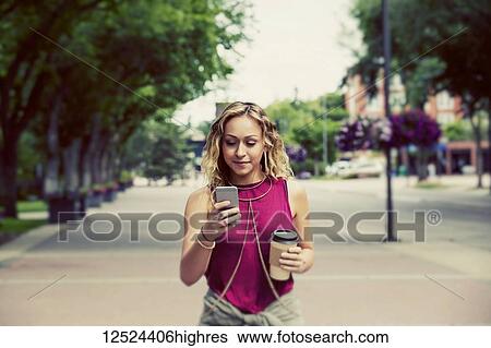 A beautiful young woman walking down a street near a university campus texting on her smart phone; Edmonton, Alberta, Canada View Large Photo Image Stock Photograph - A beautiful young woman walking down a street near a university campus texting on her smart phone; Edmonton, Alberta, Canada. Fotosearch