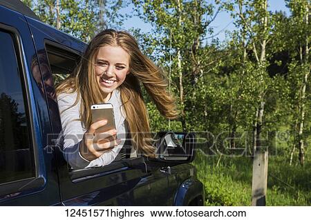 A beautiful young woman with long blond hair looking out a vehicle window and taking a self-portrait with her smart phone; Edmonton, Alberta, Canada View Large Photo Image Stock Photograph - A beautiful young woman with long blond hair looking out a vehicle window and taking a self-portrait with her smart phone; Edmonton, Alberta, Canada. Fotosearch