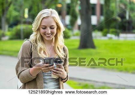 A beautiful young woman with long blond hair holding a coffee cup and texting on her smart phone while walking in a university campus; Edmonton, Alberta, Canada View Large Photo Image Stock Photograph - A beautiful young woman with long blond hair holding a coffee cup and texting on her smart phone while walking in a university campus; Edmonton, Alberta, Canada. Fotosearch