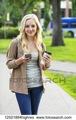 A beautiful young woman with long blond hair holding a coffee cup and texting on her smart phone while walking in a university campus; Edmonton, Alberta, Canada View Large Photo Image Stock Photograph - A beautiful young woman with long blond hair holding a coffee cup and texting on her smart phone while walking in a university campus; Edmonton, Alberta, Canada. Fotosearch