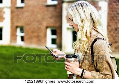 A beautiful young woman with long blond hair holding a coffee cup and texting on her smart phone while walking in a university campus; Edmonton, Alberta, Canada View Large Photo Image Stock Photograph - A beautiful young woman with long blond hair holding a coffee cup and texting on her smart phone while walking in a university campus; Edmonton, Alberta, Canada. Fotosearch