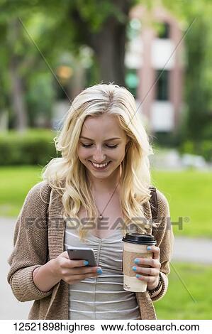 A beautiful young woman with long blond hair holding a coffee cup and texting on her smart phone while walking in a university campus; Edmonton, Alberta, Canada View Large Photo Image Stock Photograph - A beautiful young woman with long blond hair holding a coffee cup and texting on her smart phone while walking in a university campus; Edmonton, Alberta, Canada. Fotosearch