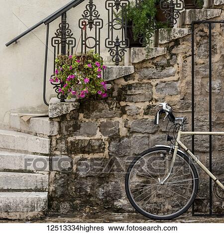 Stock Photograph - A bicycle parked beside a stone wall with steps leading up and plants decorating the railing; Budva, Opstina Budva, Monte. Fotosearch